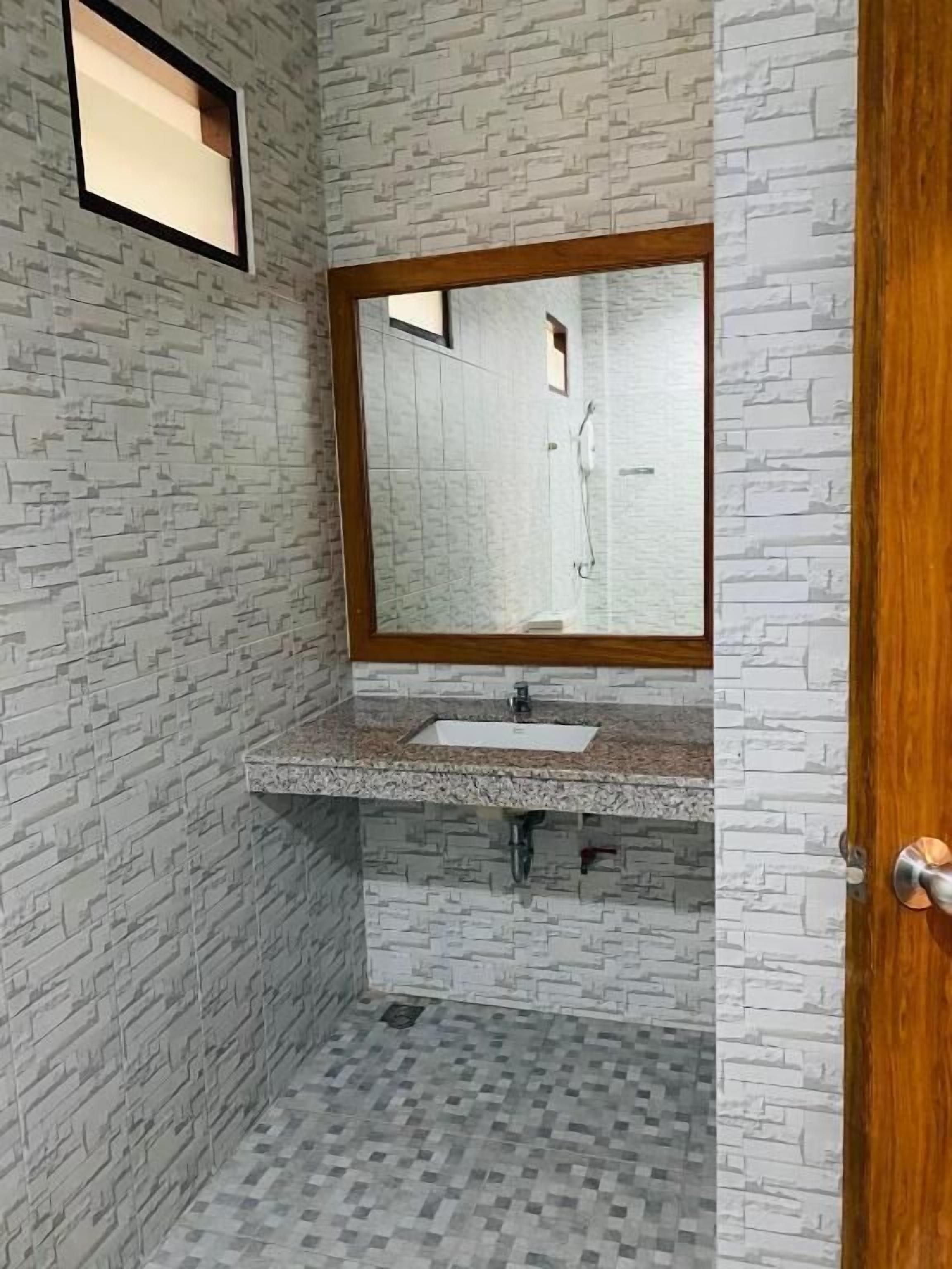 A bathroom with a stone-textured wall, a wooden-framed mirror, a granite countertop, and a tiled floor.