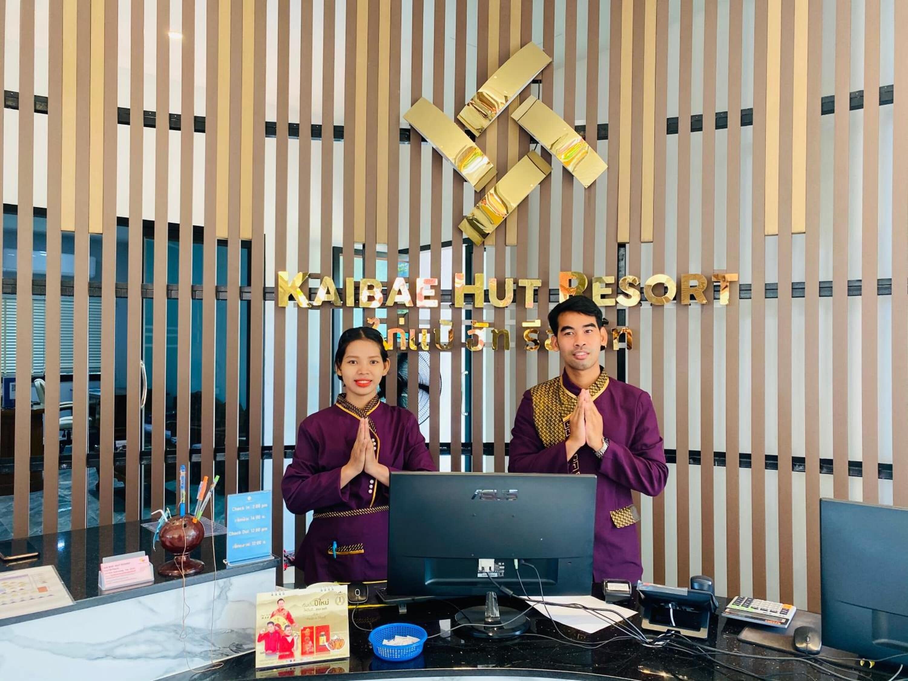 A reception desk at Kaibae Hut Resort with two staff members standing behind it, a computer, and various office supplies.
