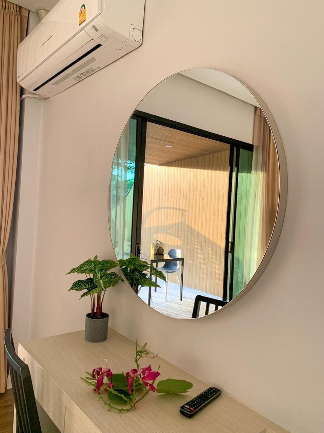 Una habitación con un espejo redondo, una planta en maceta, un control remoto y una mesa de comedor.