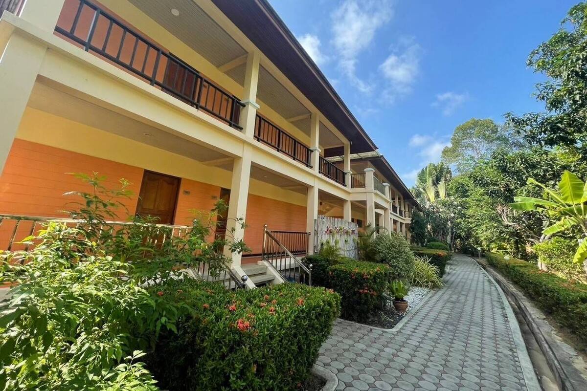 Un hotel de varios pisos con balcones, un camino pavimentado y abundante vegetación.