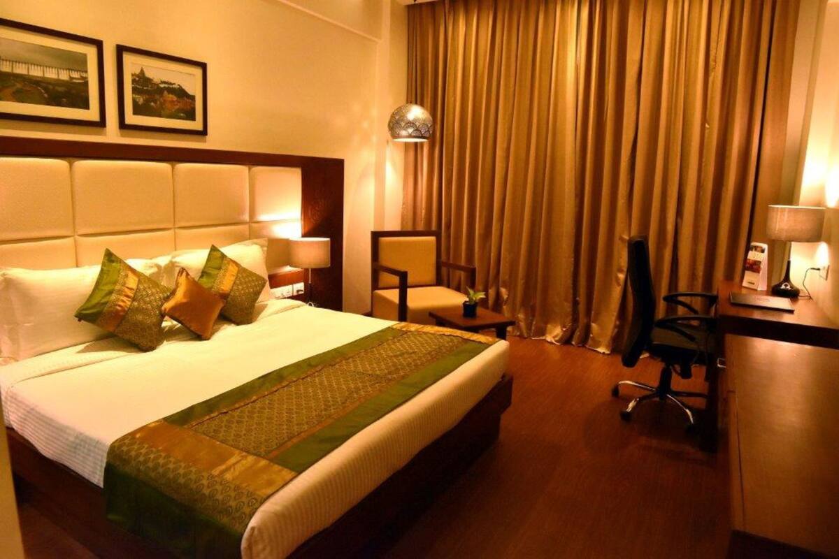 A hotel room with a large bed, a desk, a chair, and a lamp.