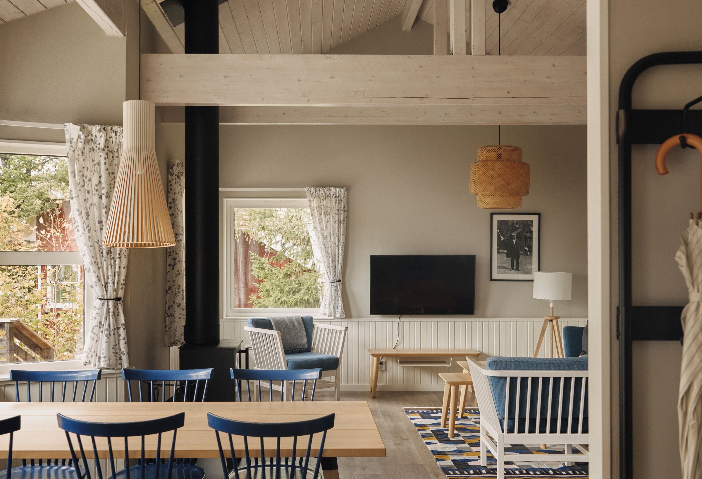 Ein gemütliches Zimmer mit Holzboden, einem an der Wand montierten Fernseher und einer Essecke mit blauen Stühlen und einem Holztisch.