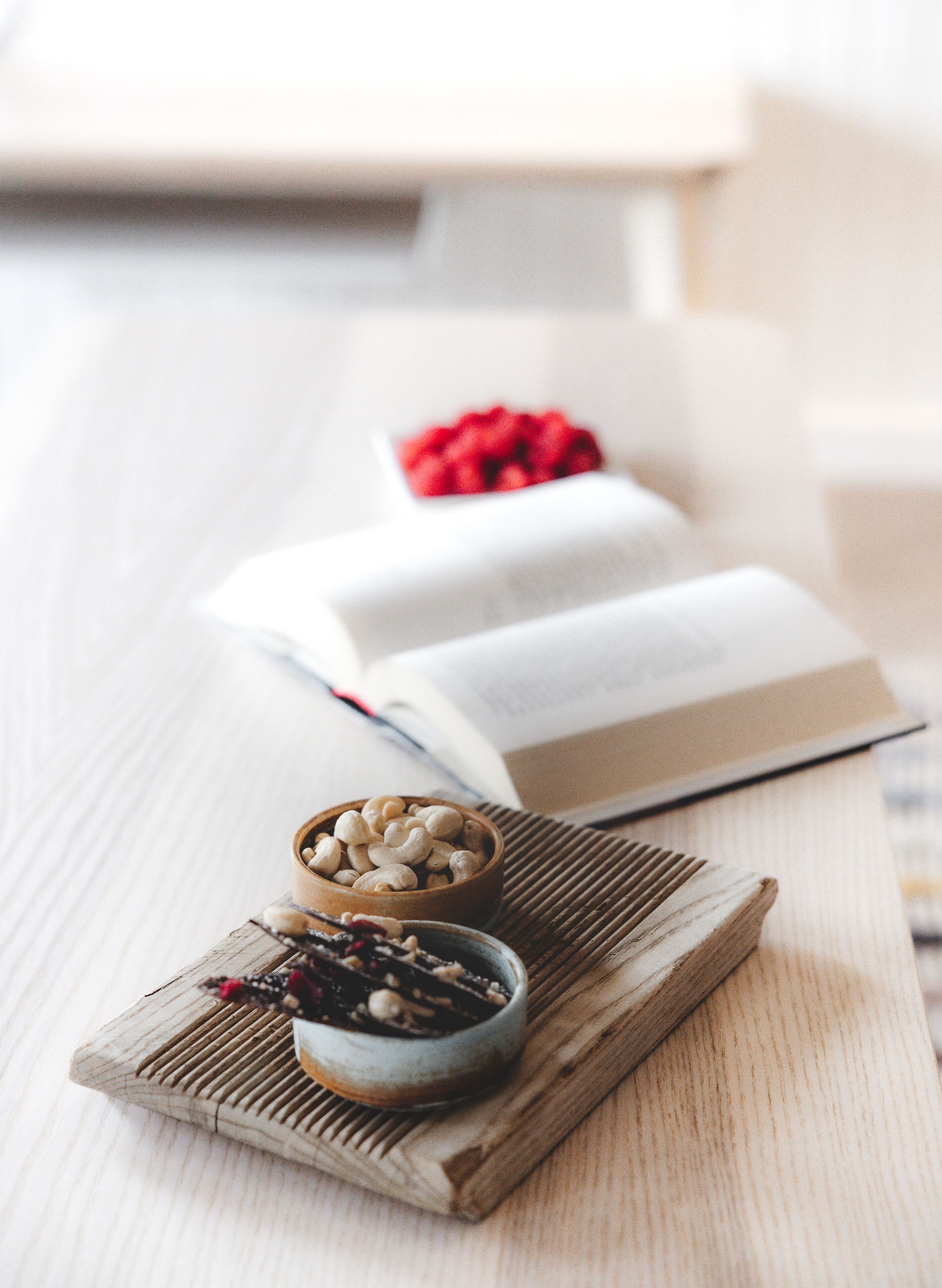Una mesa de madera con un tazón de anacardos, un tazón de frutas secas y un libro.