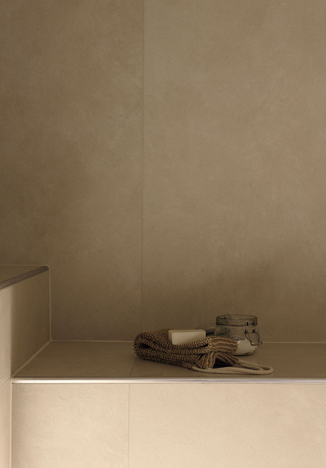 A bathroom with a towel, soap, and a glass jar on a shelf.
