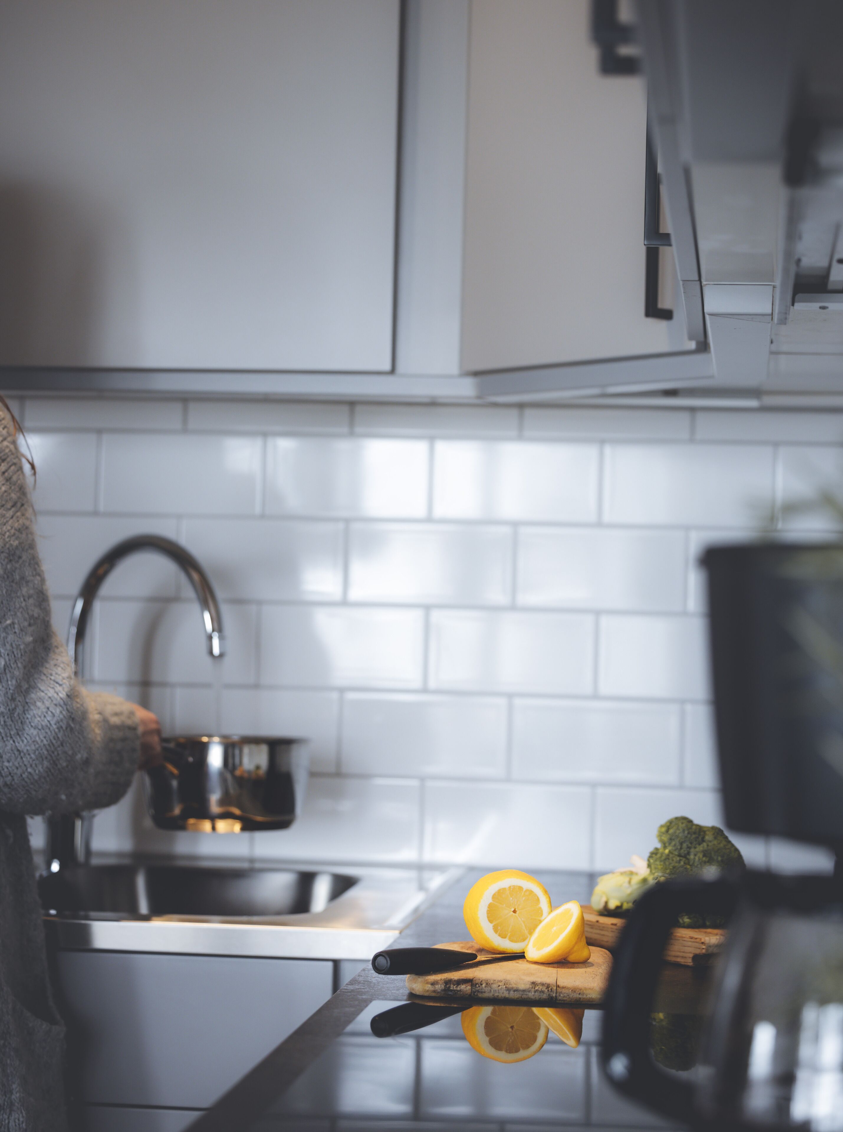 A kitchen with white cabinets, a stainless steel sink, and a cutting board with citrus fruits.