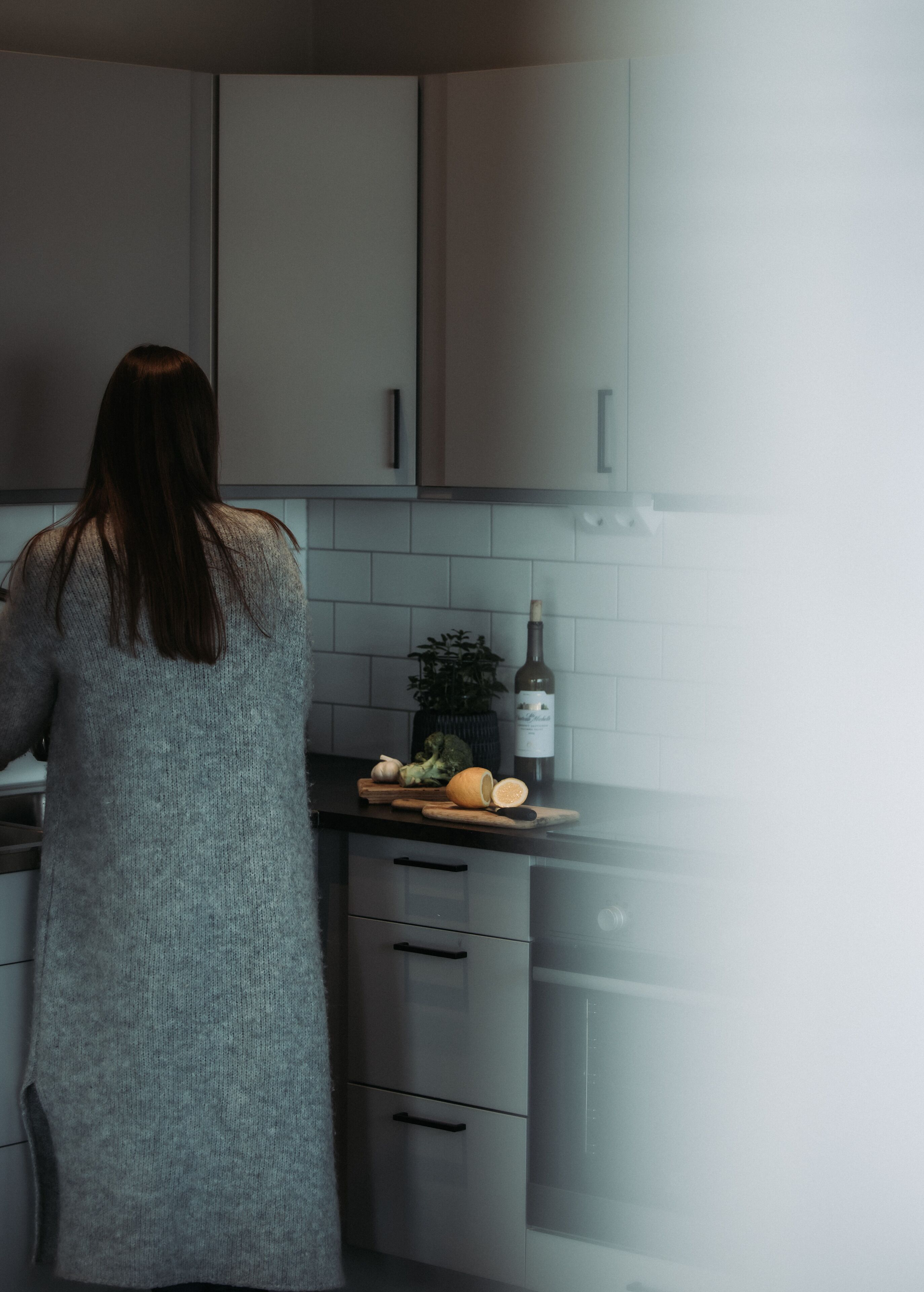 Een keuken met grijze kastjes, een aanrecht met een fles wijn en een plant.