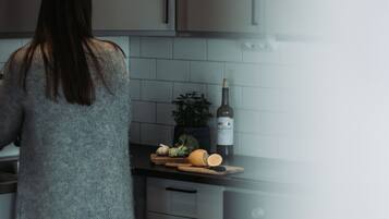 Een keuken met grijze kastjes, een aanrecht met een fles wijn en een plant.