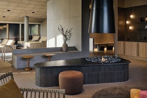 Un vestíbulo moderno con una zona de estar central, una chimenea y una cocina al fondo.