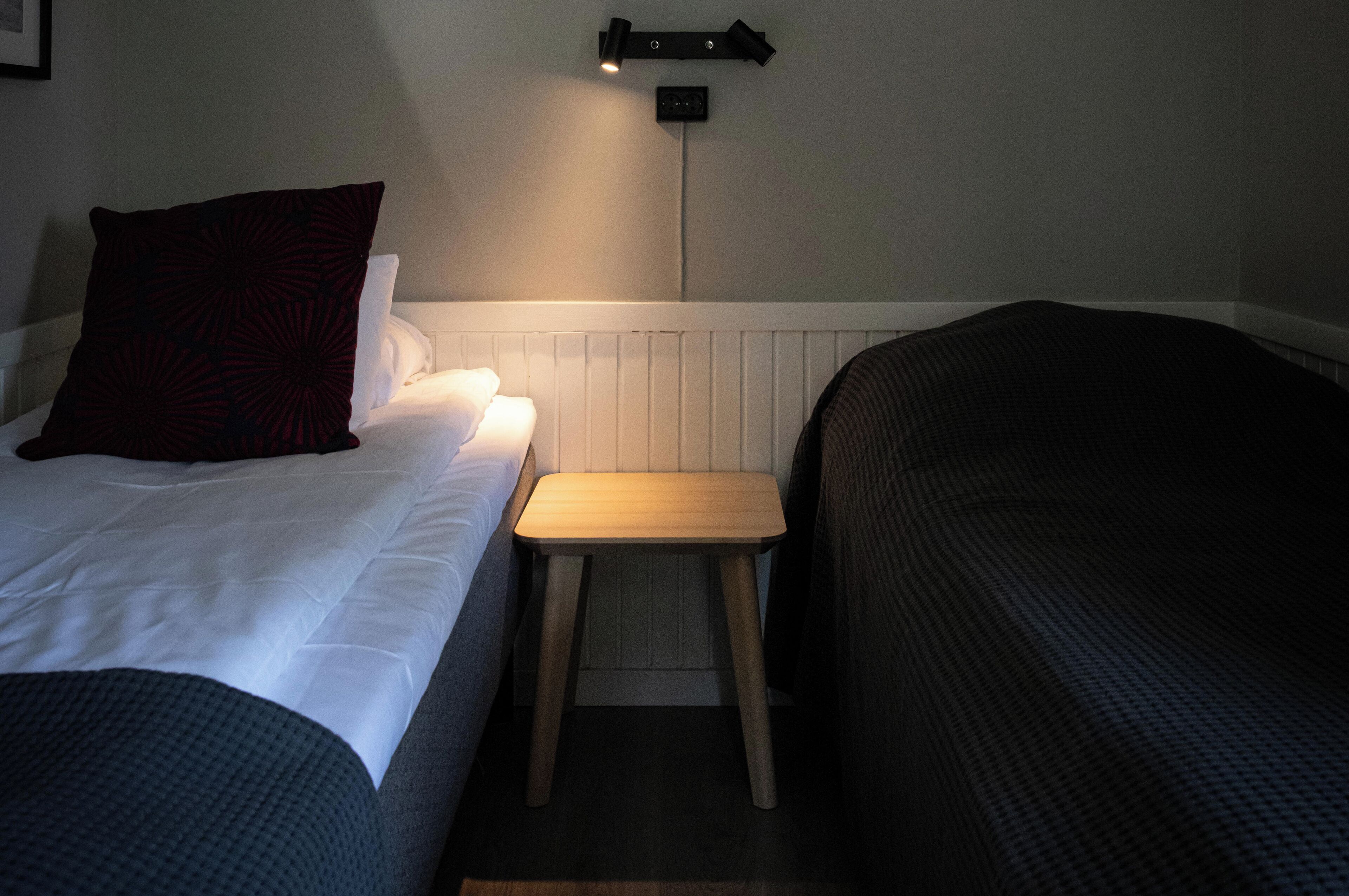 Et hotelværelse med to senge, et lille trænatbord og en vægmonteret lampe.