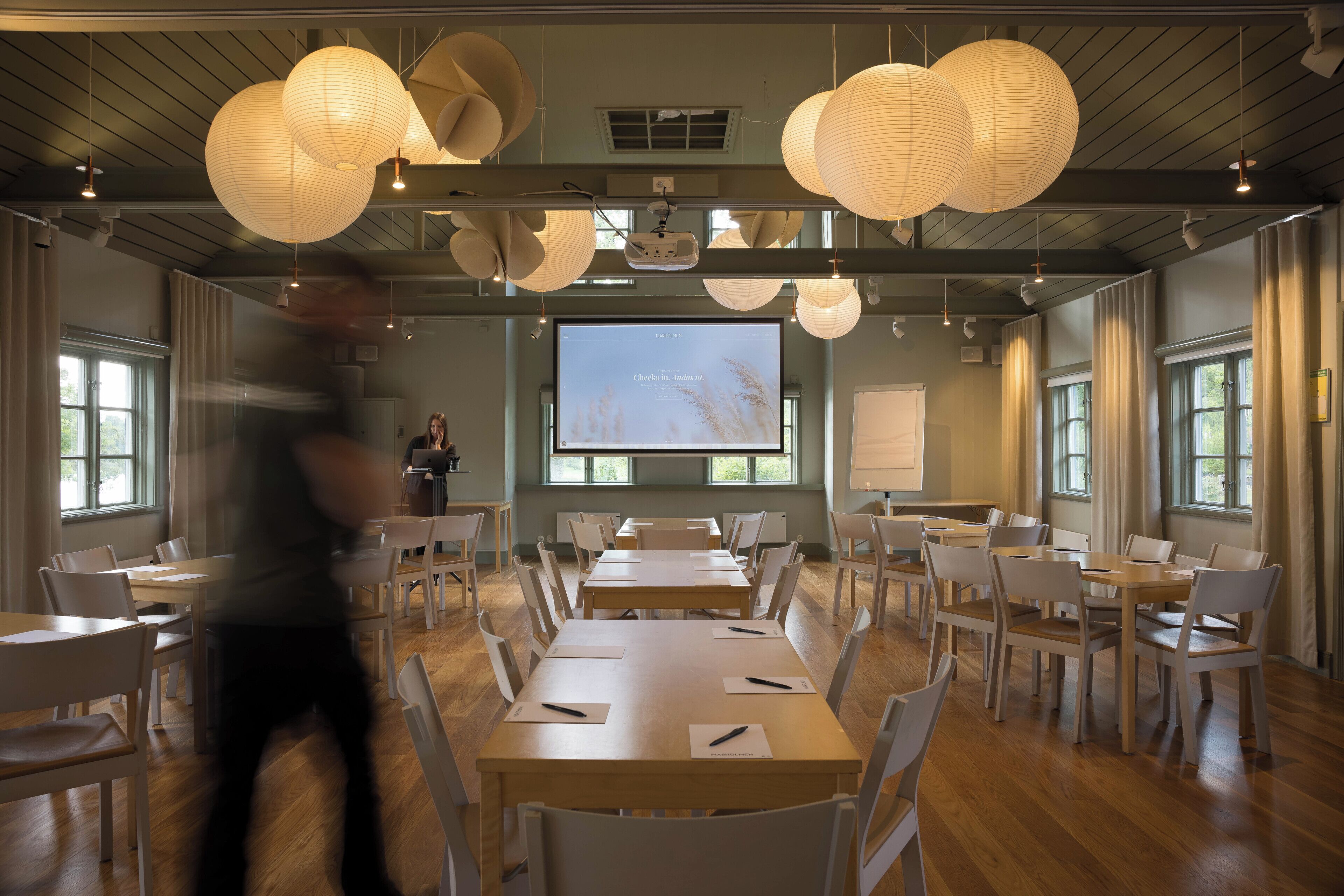 A conference room with tables and chairs, a projector screen, and hanging paper lanterns.