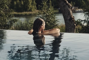 Una persona en una piscina cristalina con vista a un lago y árboles.