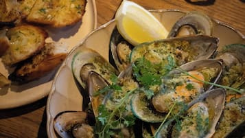 Ein Teller mit gekochten Muscheln, garniert mit Kräutern und Zitronenscheiben, zusammen mit geröstetem Brot auf einer Holztischplatte.