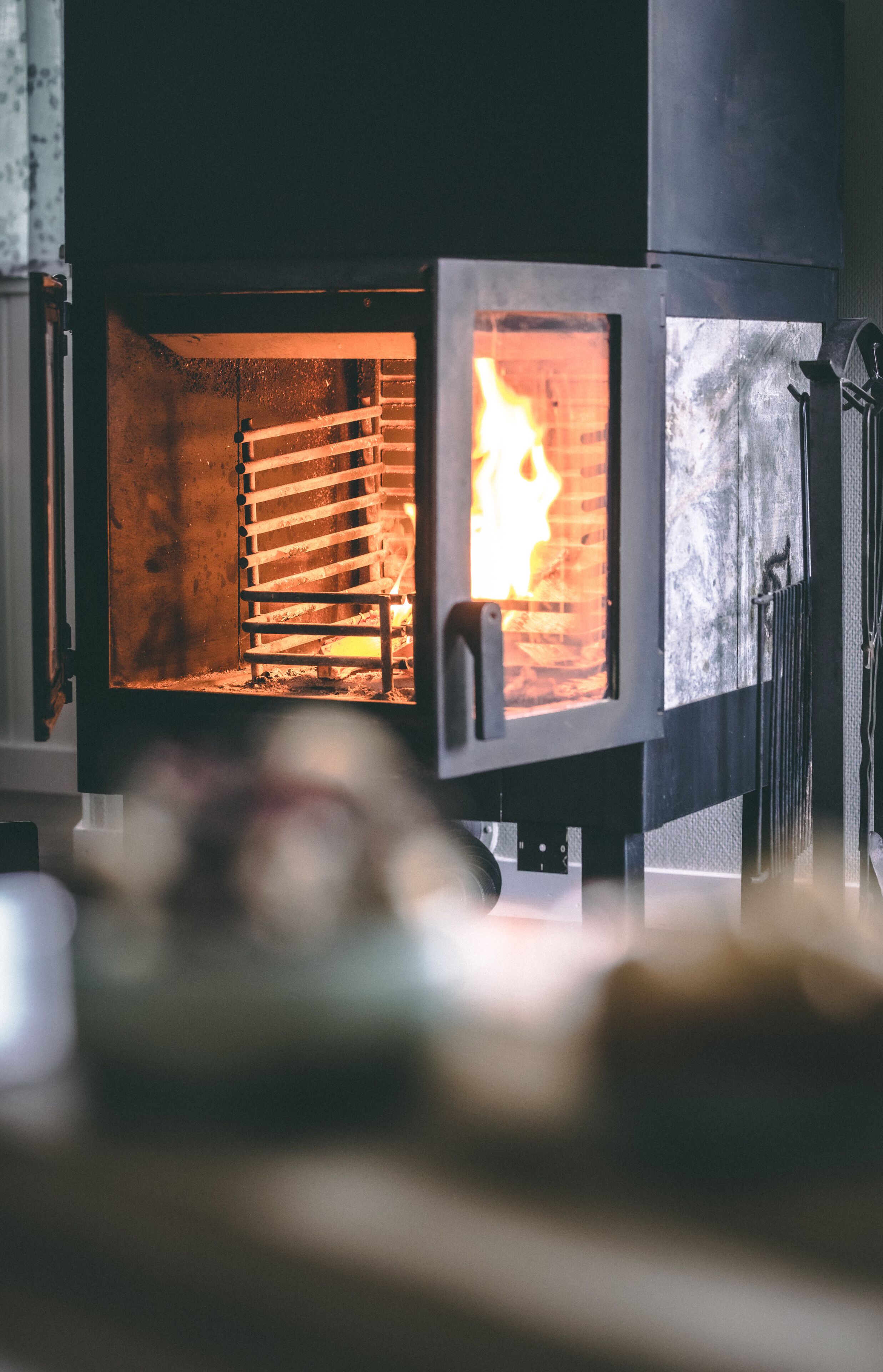 En vedeldad kamin med synliga lågor inuti, ett metallgaller och en glaslucka.