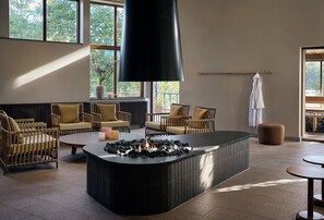 A modern lounge area with wicker furniture, a central fire feature, and large windows providing natural light. - Marholmen Stugor (Norrtälje)