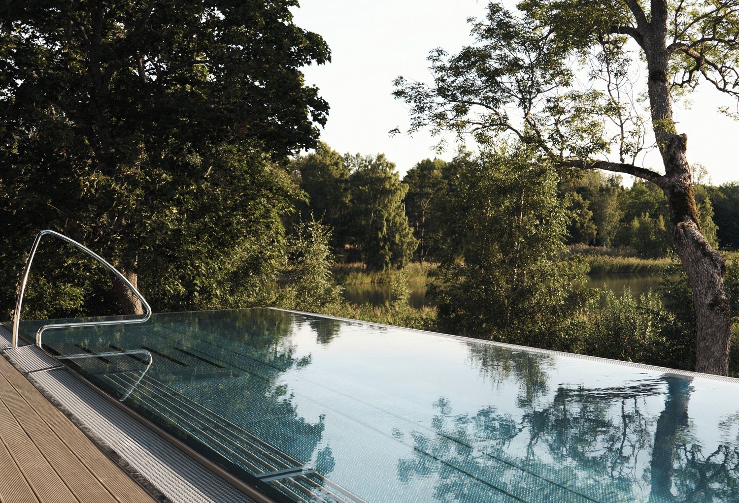 An outdoor infinity pool with a clear view of the surrounding trees and a calm body of water.