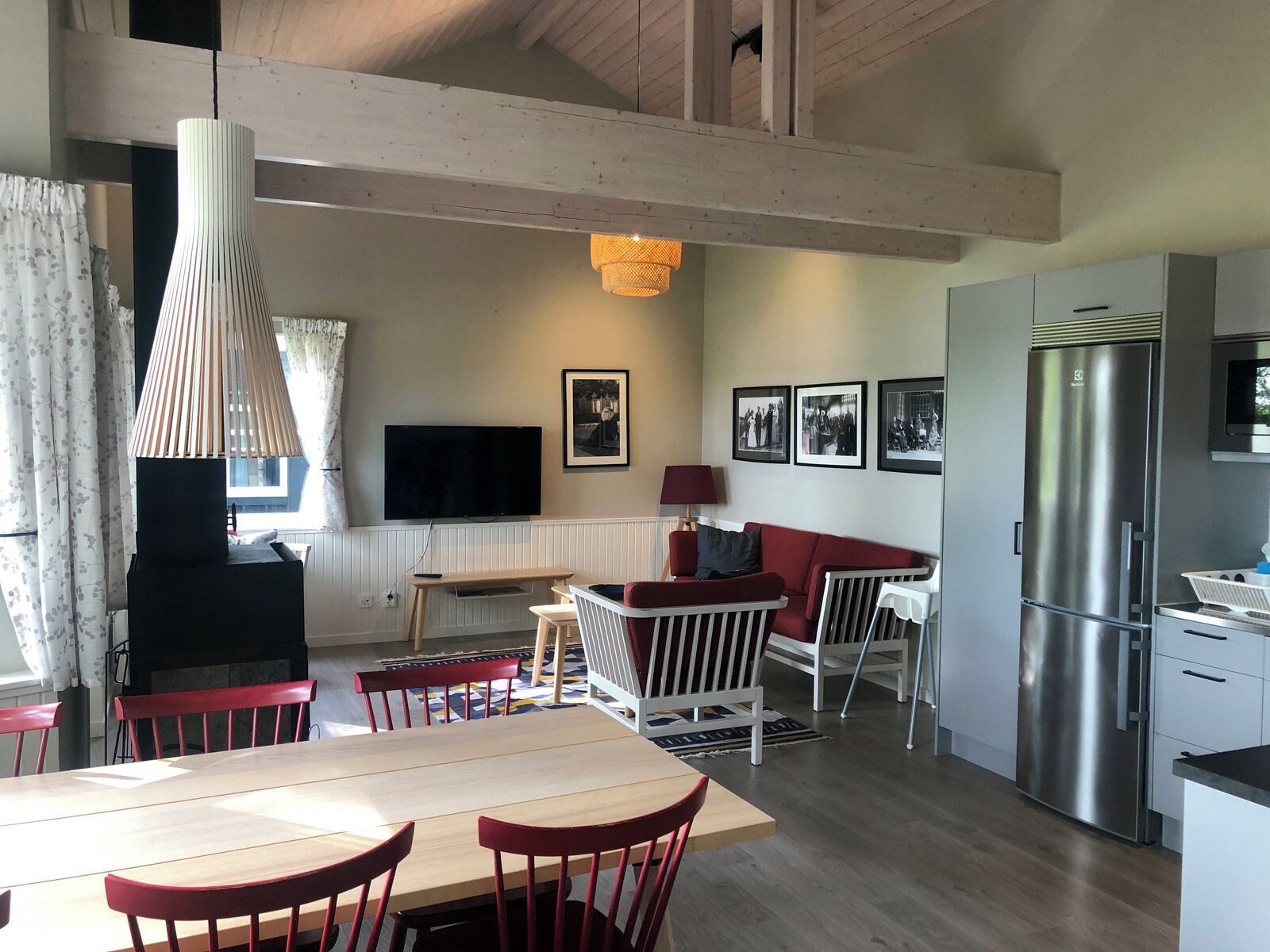 A modern kitchen with a built-in refrigerator, a dining area with a wooden table and red chairs, and a living area with a sofa and a TV.