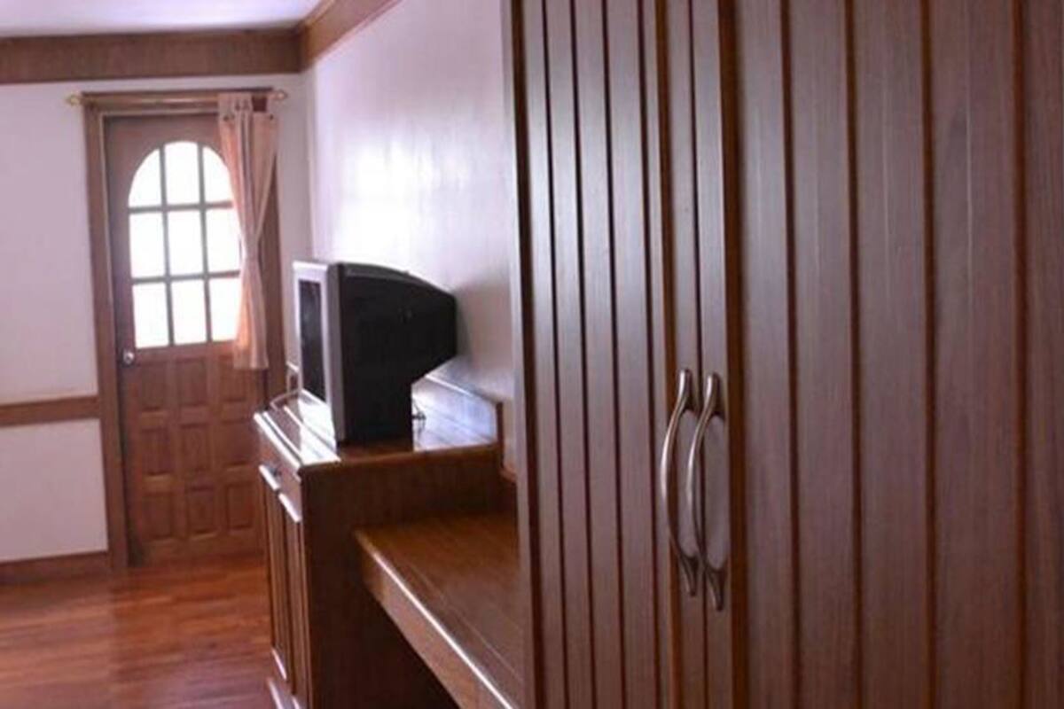 A room with wooden flooring, a wooden door, a window with curtains, and a wooden cabinet with a handle.