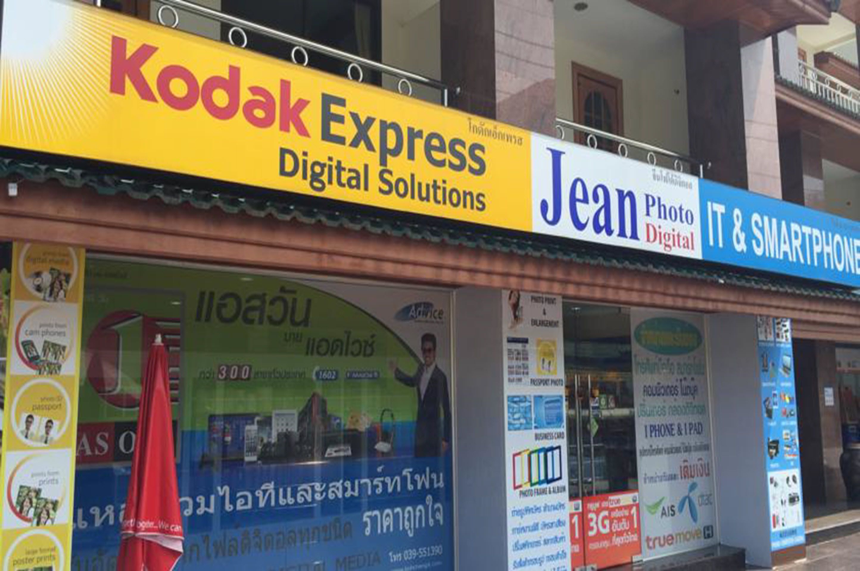 A storefront with signs for Kodak Express Digital Solutions and Jean Photo Digital IT & Smartphone services.