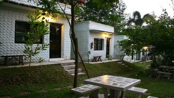A white building with textured walls, a door, and windows. There are outdoor tables and benches.