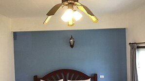 Un dormitorio con cama, ventilador de techo, lámpara de pared y ventana con cortinas.