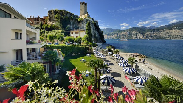 Un hotel costero con un castillo en un acantilado, una playa con sombrillas y una vista despejada del mar.