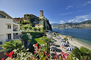 A coastal hotel with a castle on a cliff, a beach with umbrellas, and a clear view of the sea. - Hotel Castello Lake Front (Malcesine)
