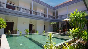 A courtyard with a swimming pool, multiple seating areas, and a covered seating area with umbrellas. - Teges Inn Kuta (Kuta)