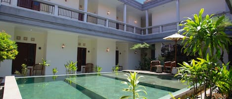 A courtyard with a swimming pool, multiple seating areas, and a covered seating area with umbrellas.