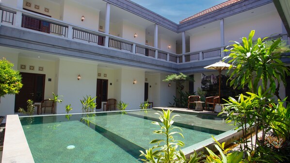 A courtyard with a swimming pool, multiple seating areas, and a covered seating area with umbrellas. - Teges Inn Kuta (Kuta)