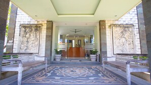 A reception area with a reception desk, two potted plants, and a patterned carpet. - Teges Inn Kuta (Kuta)