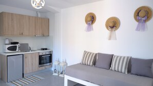 A modern kitchen with wooden cabinets, a microwave, and a refrigerator. There is a white sofa with striped pillows and a small table with a vase. - Axos Apartments (Hersonissos)