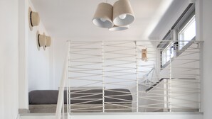 A staircase with a metal railing, a striped sofa with cushions, and a ceiling light fixture. - Axos Apartments (Hersonissos)