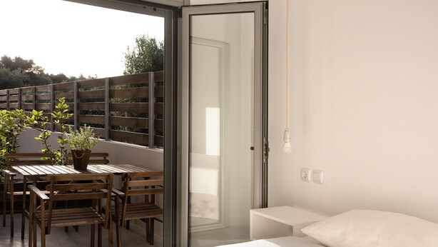 A modern room with a bed, a wooden table with chairs, and a potted plant. - Axos Apartments (Hersonissos)