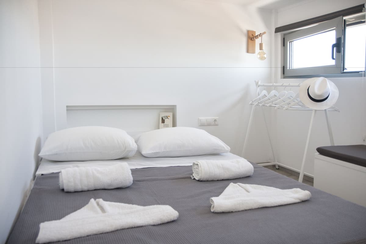Una cama bien tendida con almohadas y toallas blancas, una lámpara de noche y una ventana con vistas.