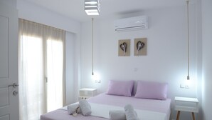 A bedroom with a bed, two bedside tables, an air conditioning unit, and a window with curtains. - Axos Apartments (Hersonissos)