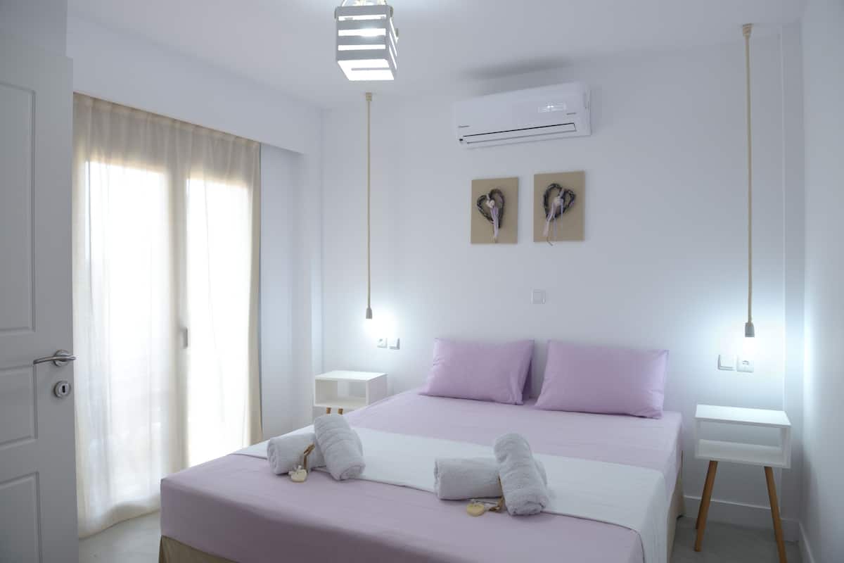 Un dormitorio con cama, dos mesitas de noche, aire acondicionado y ventana con cortinas.