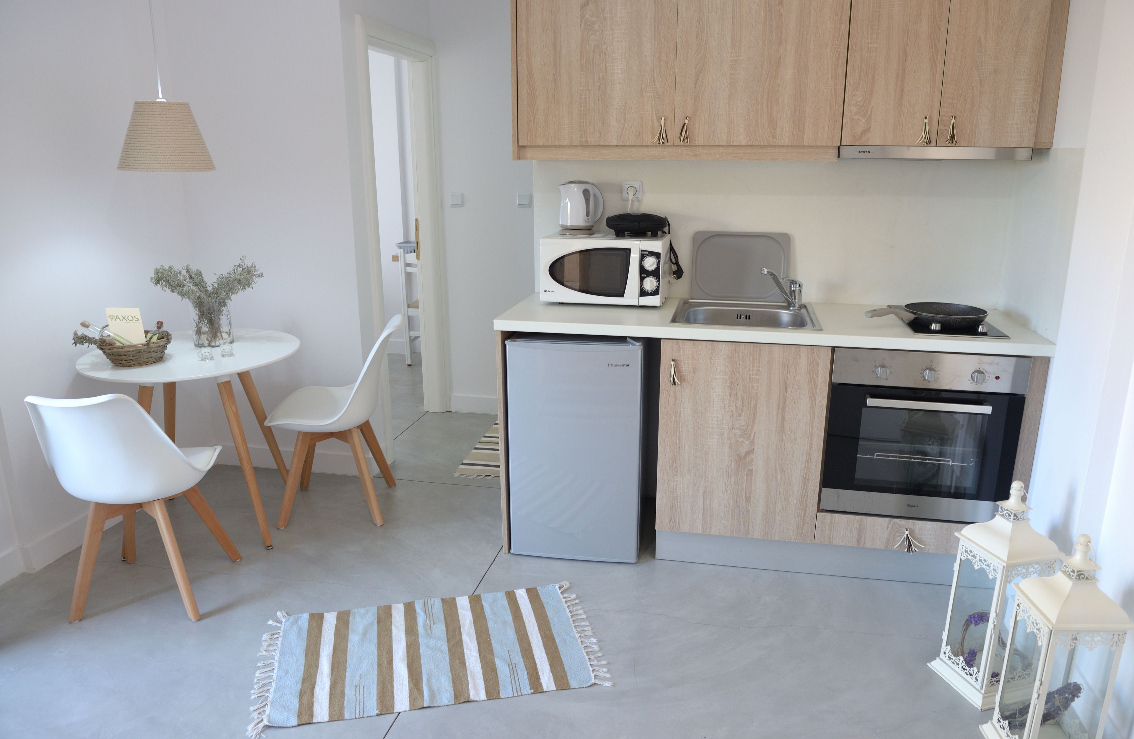 A compact kitchen with a microwave, toaster, sink, and oven. There is a small refrigerator, a dining table with chairs, and a decorative rug.