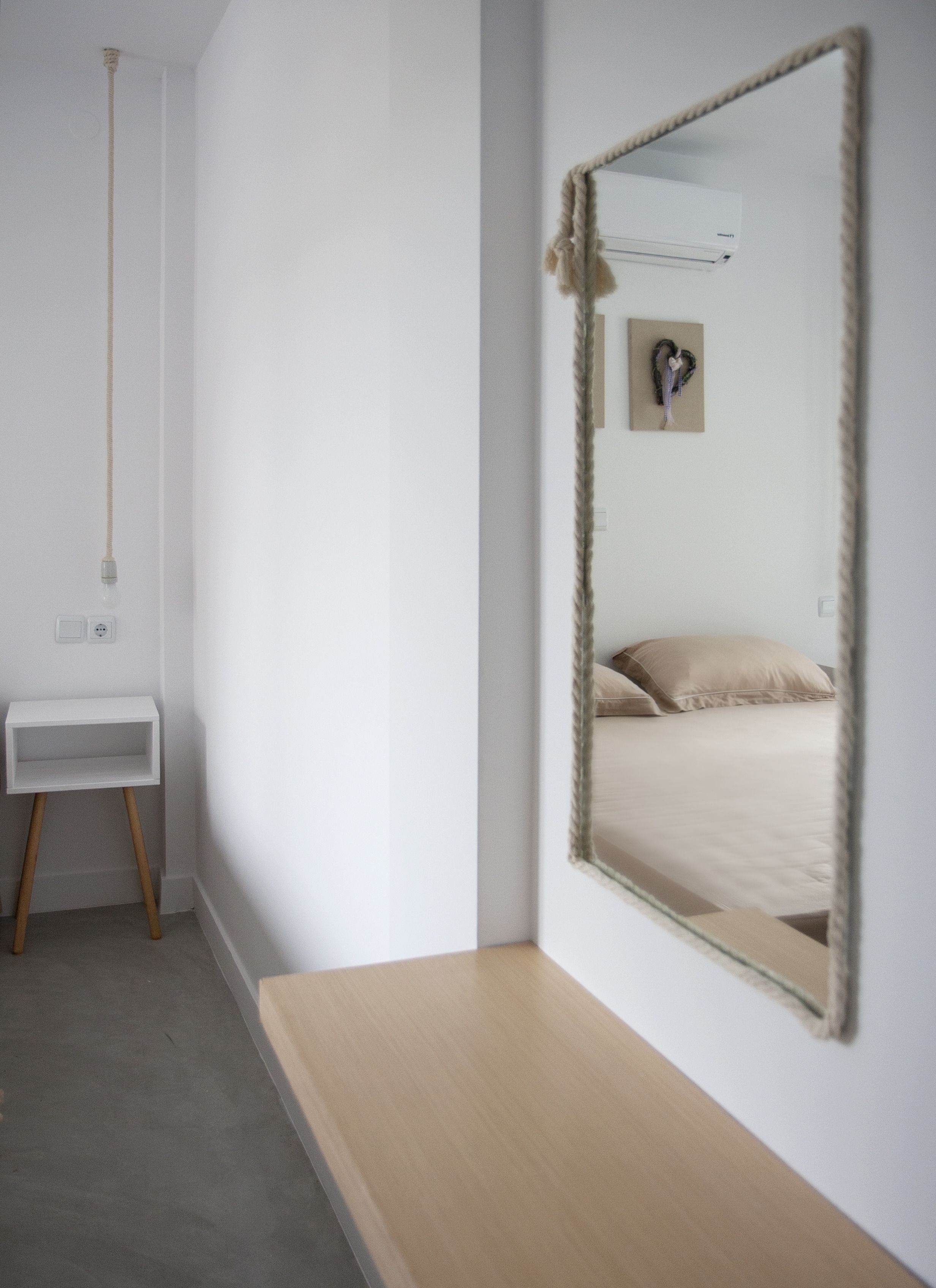 A minimalist bedroom with a wooden bedside table, a large mirror, and a bed with beige bedding.