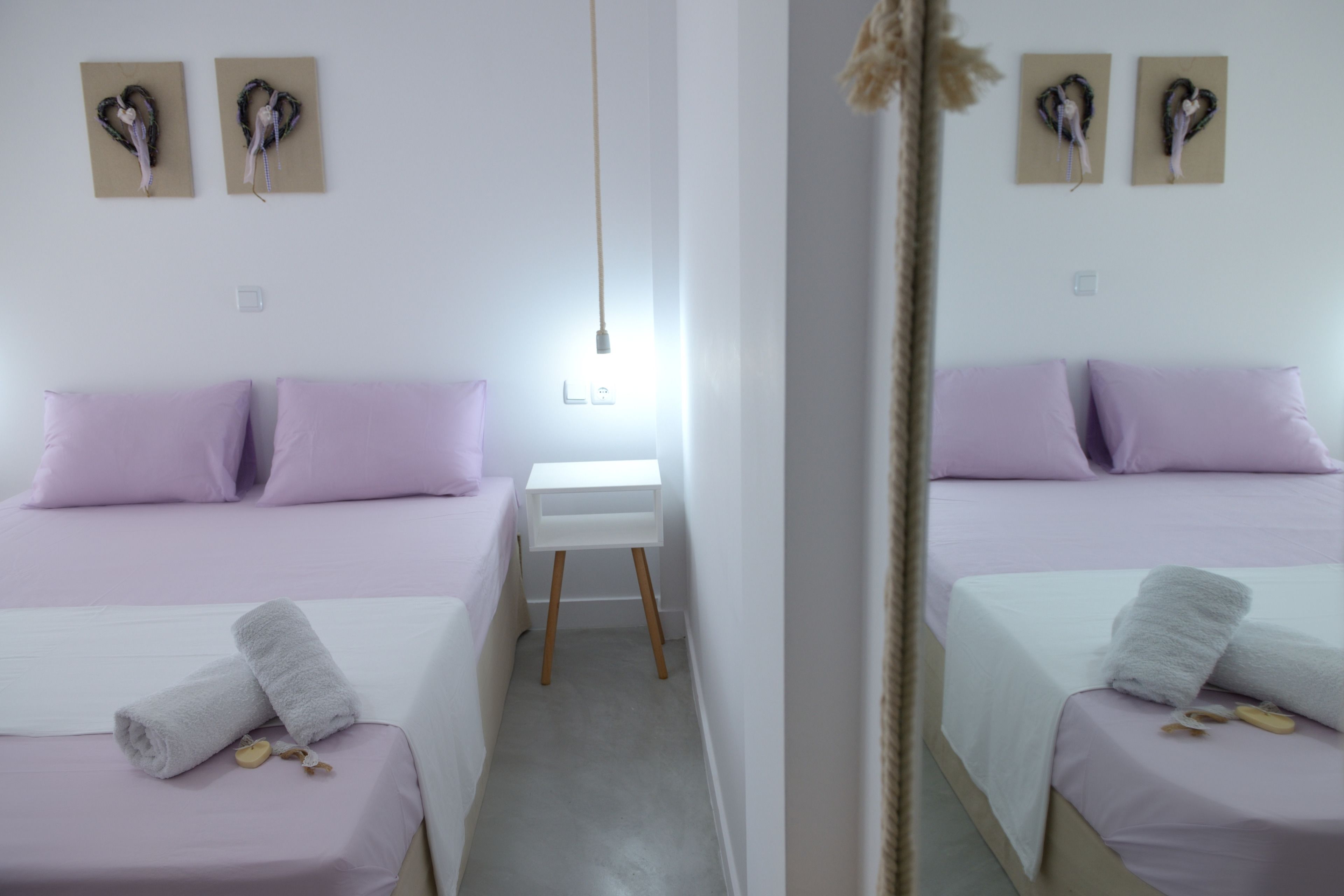 Ein Hotelzimmer mit zwei Betten, jeweils mit einer weißen und lavendelfarbenen Tagesdecke, und einem kleinen weißen Nachttisch dazwischen.