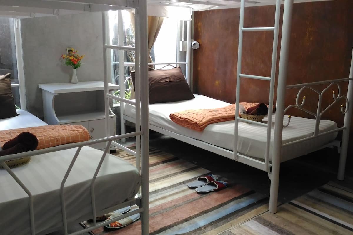 Un dormitorio con literas, una mesita pequeña, un florero con flores y una ventana con cortinas.