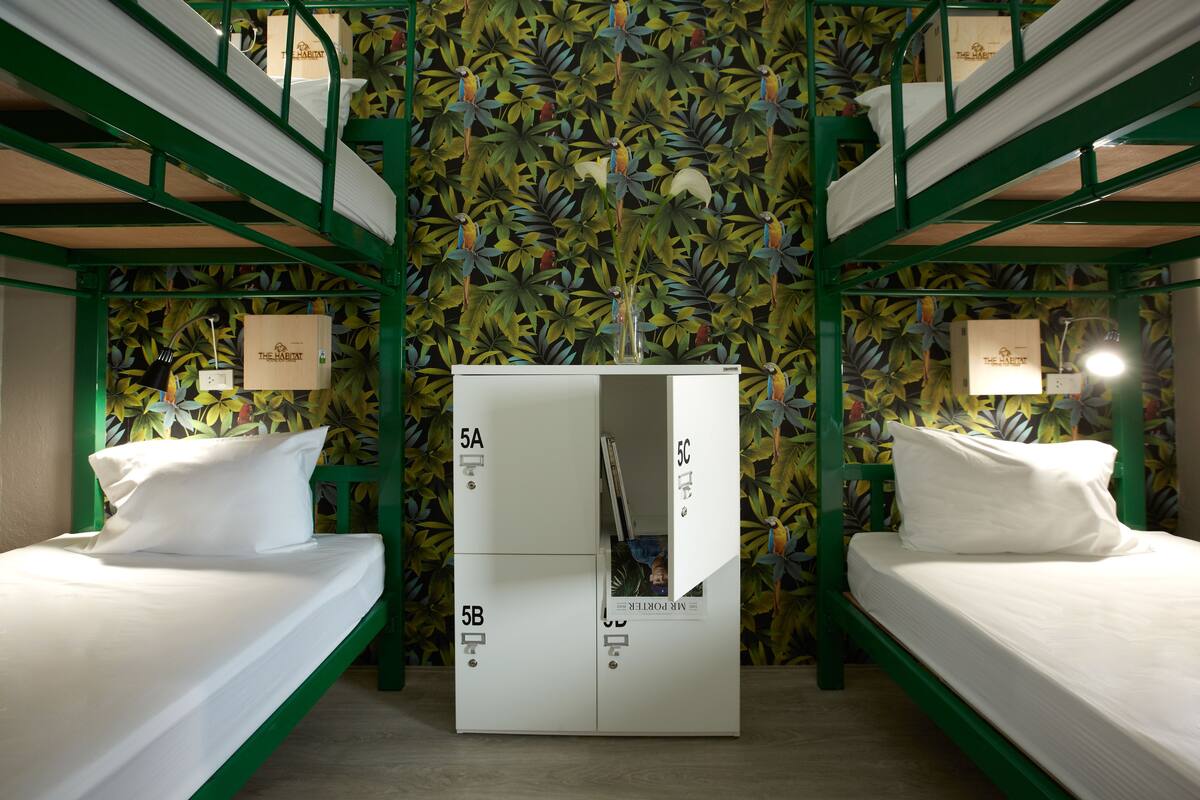 Een kamer met stapelbedden, een centraal meubel met vakken, gelabeld 5A, 5B en 5C, en bloemenbehang.