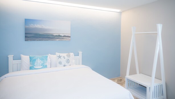 Une chambre à coucher avec un lit, un baldaquin blanc, un tableau représentant une plage et une petite étagère blanche.
