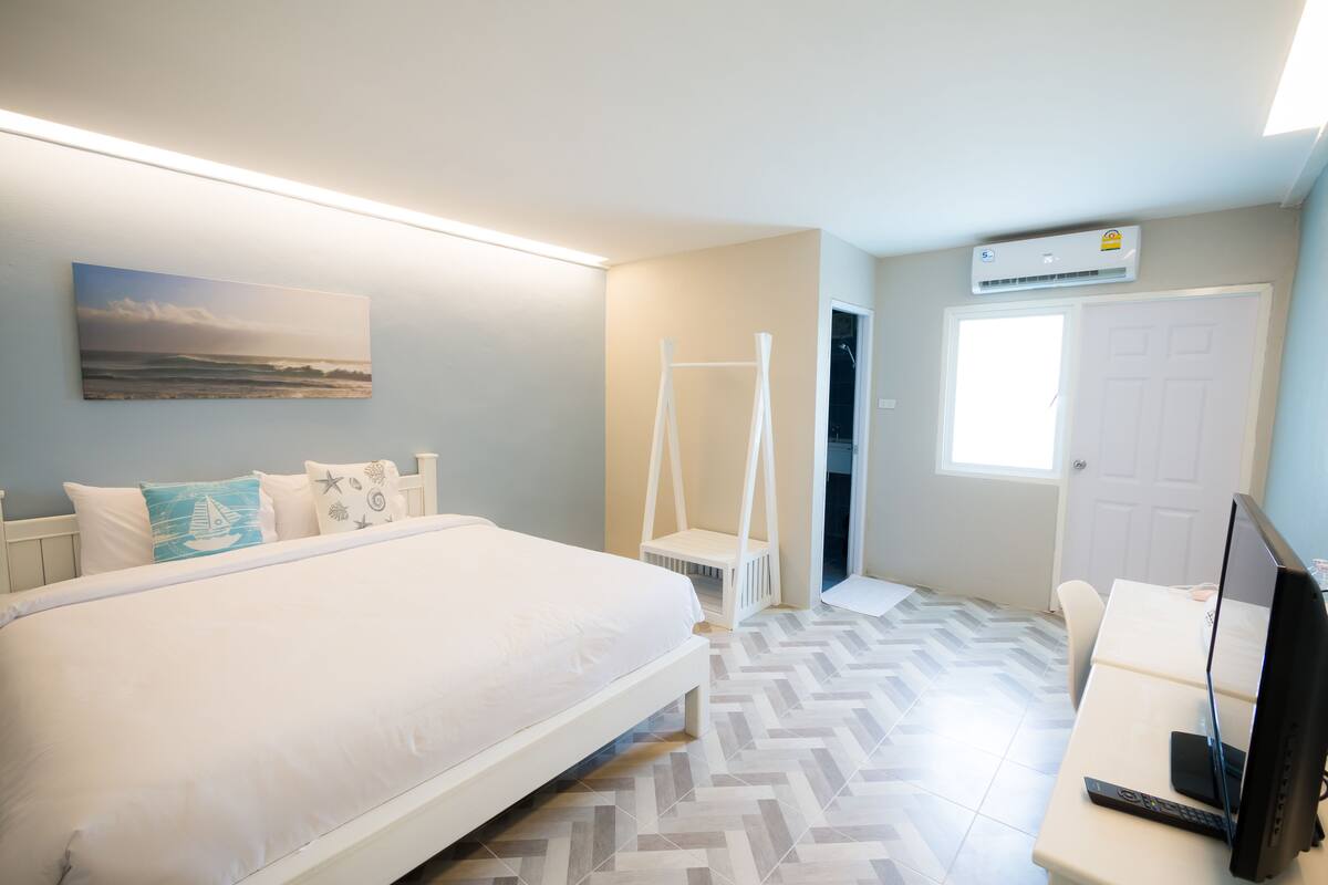 Een slaapkamer met een bed, een bureau met een computer, een raam en een airconditioning.