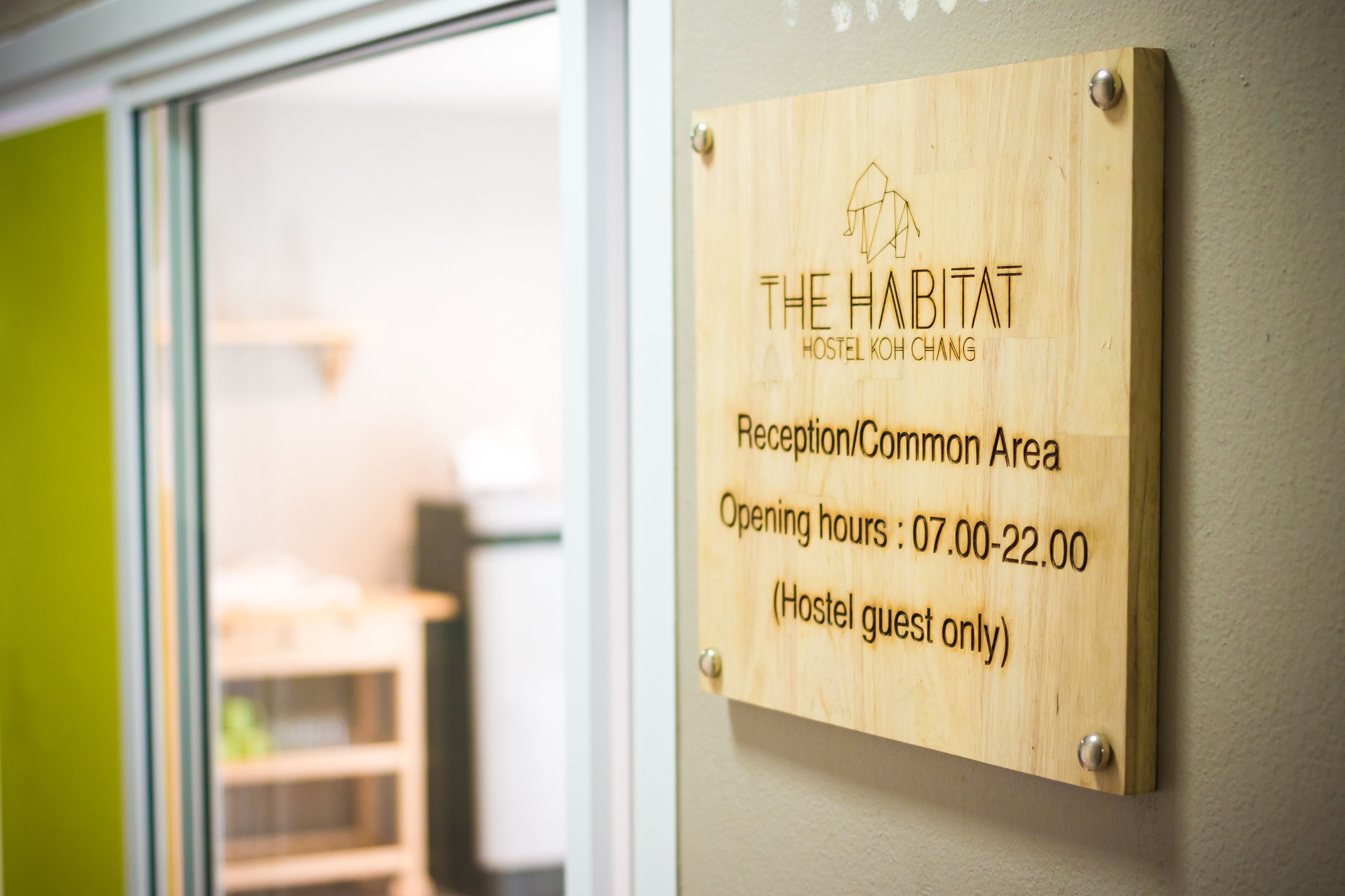 A wooden sign indicating 'The Habitat Hostel Koh Chang' Reception/Common Area with opening hours from 07:00 to 22:00, designated for hostel guests only.