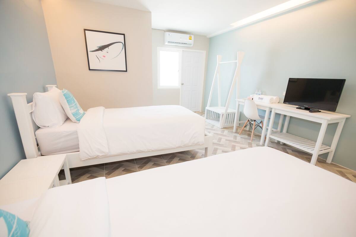 Een hotelkamer met twee bedden, een bureau met een televisie, een stoel en een schilderij aan de muur.
