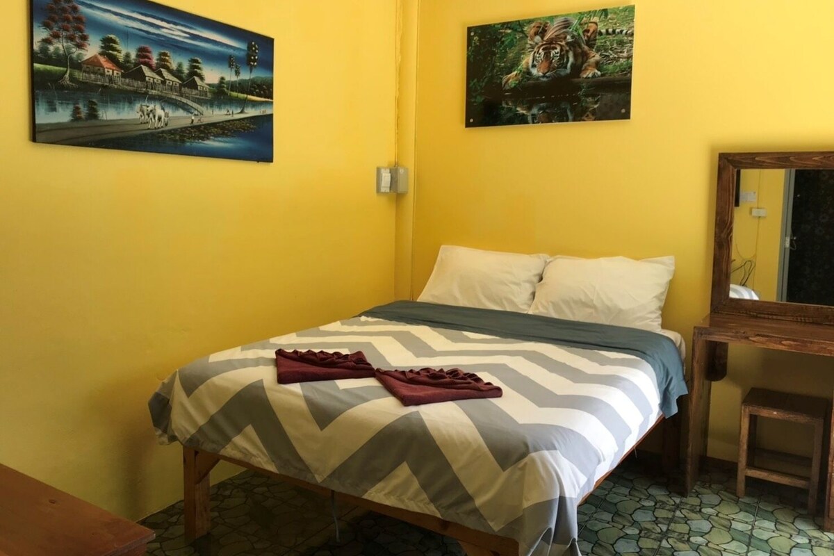 Een kamer met een bed, een houten nachtkastje, een spiegel en twee schilderijen aan de muur.