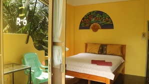 A room with a bed, a green chair, a small table, and a painting on the wall. - Island Lodge (Ko Chang)