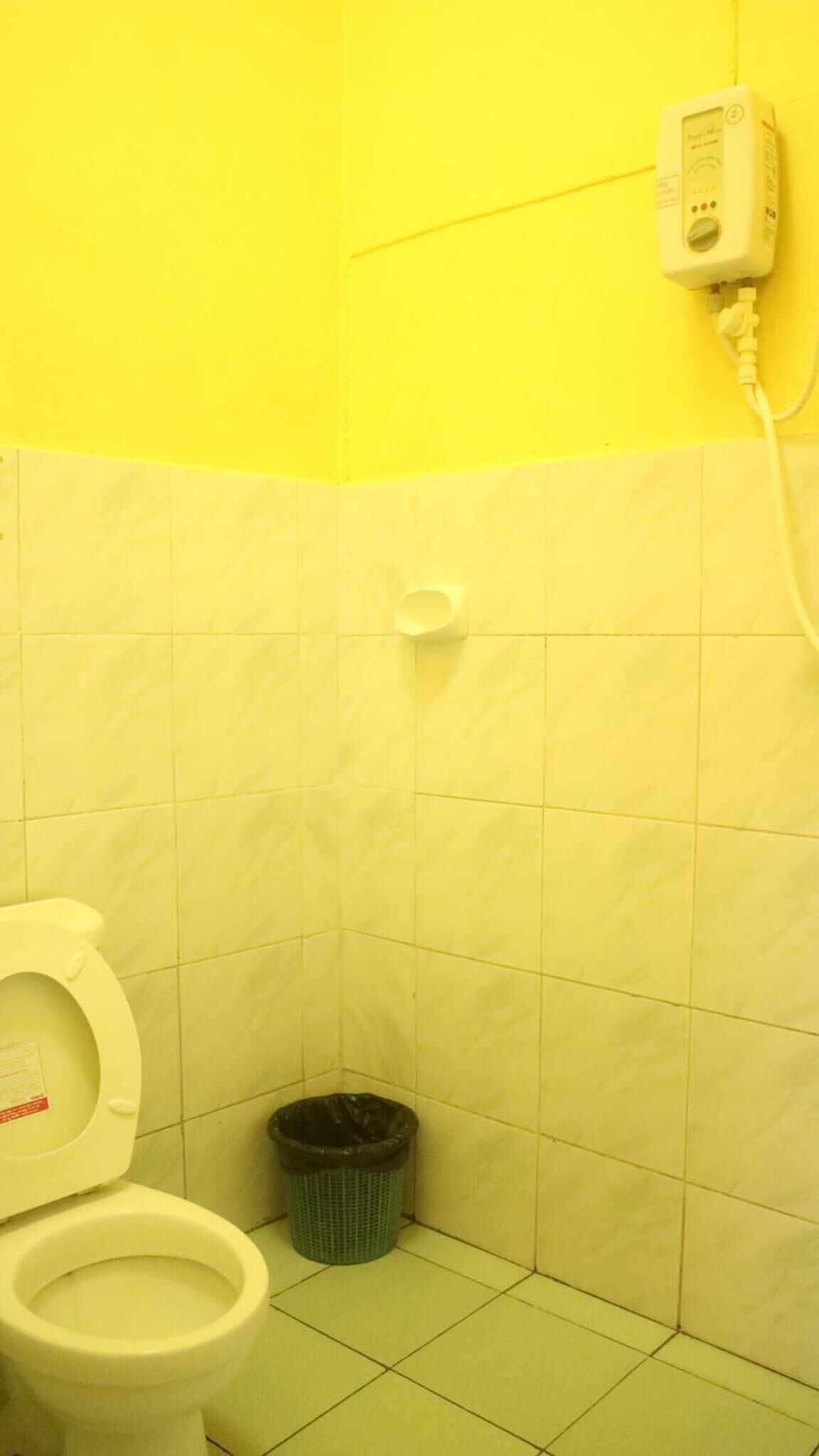 A small bathroom with yellow walls and a white toilet. There is a trash bin and a hand dryer on the wall.