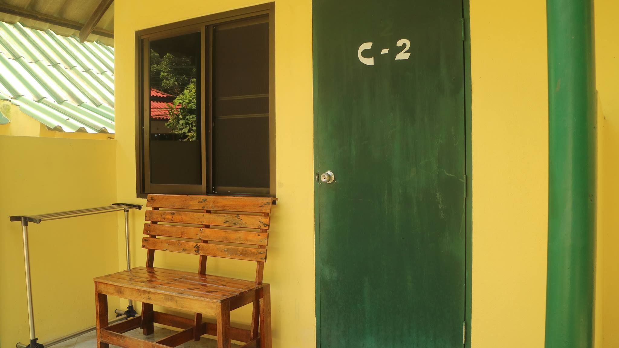 A green door with the number 2, a wooden bench, and a window with a view of a red-roofed building.