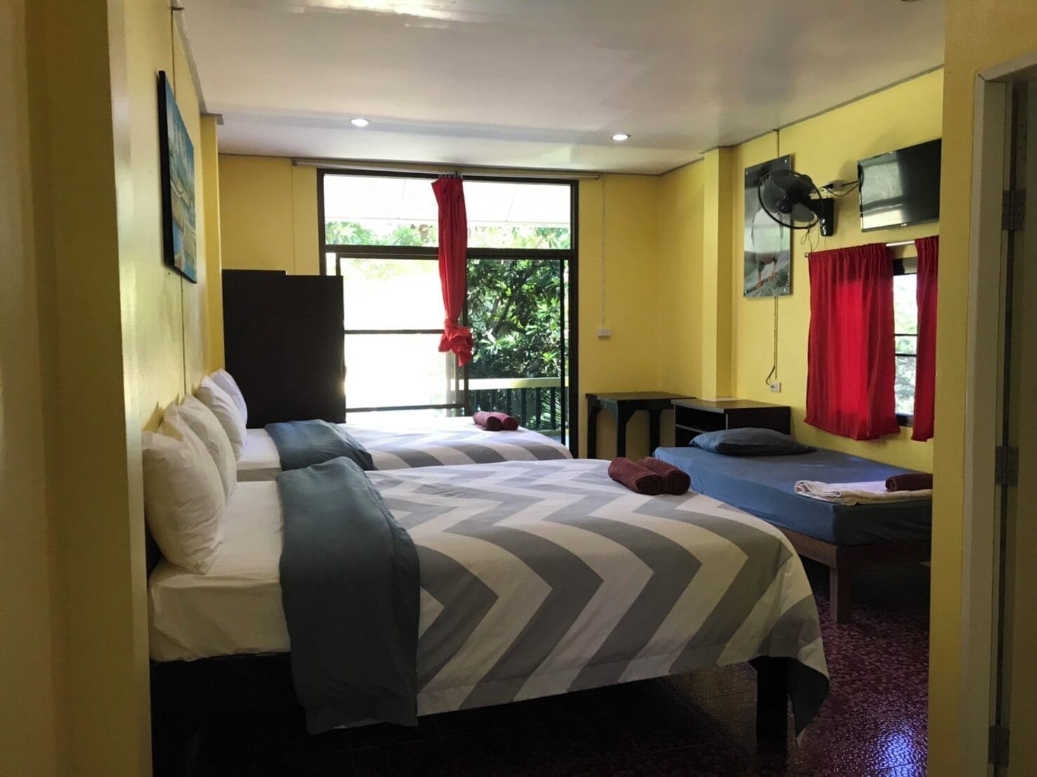 A room with two beds, a TV, and a window with red curtains.